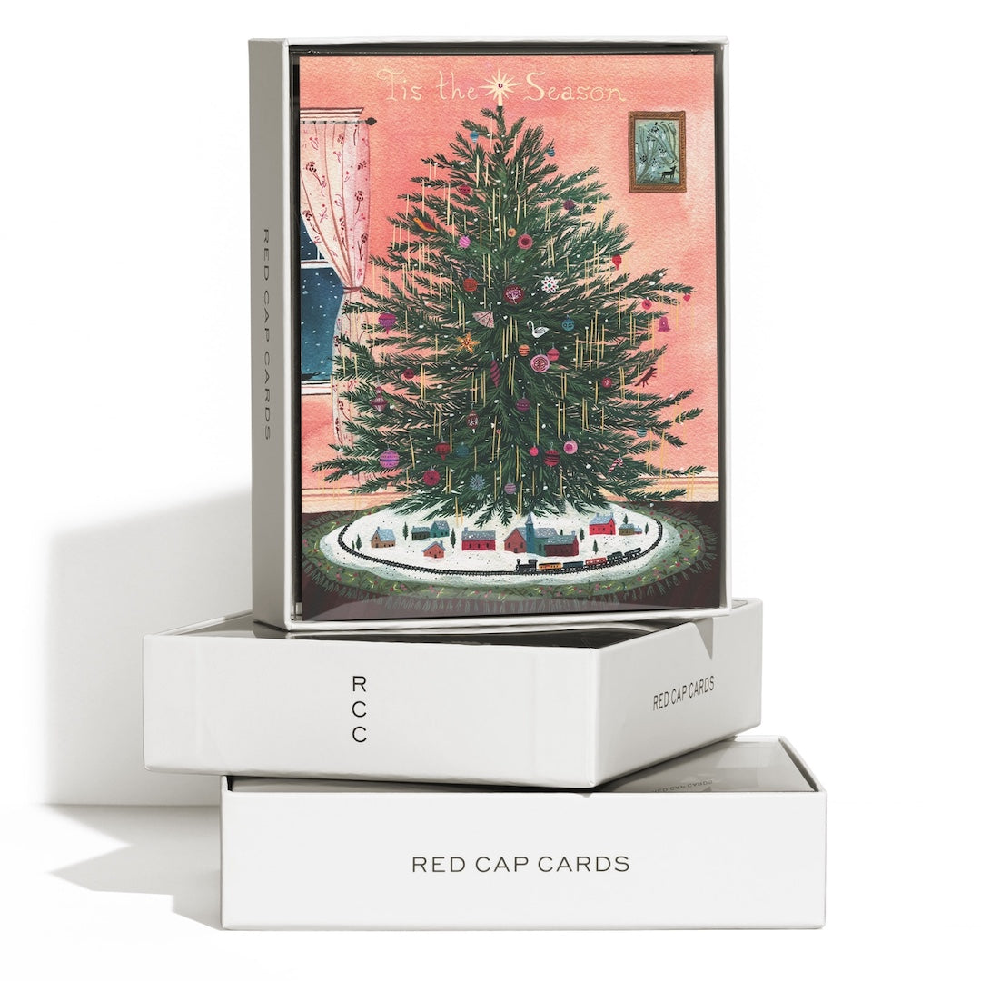 A boxed greeting card set displayed on a white surface against a white background. The top box shows a vintage-style illustration of a Christmas tree with a pink background and the text 'It is the Season.