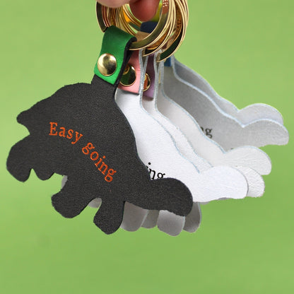 Close-up of a tortoise shaped keyring  attached to gold key rings. The front black tag has orange text reading 'Easy going'.