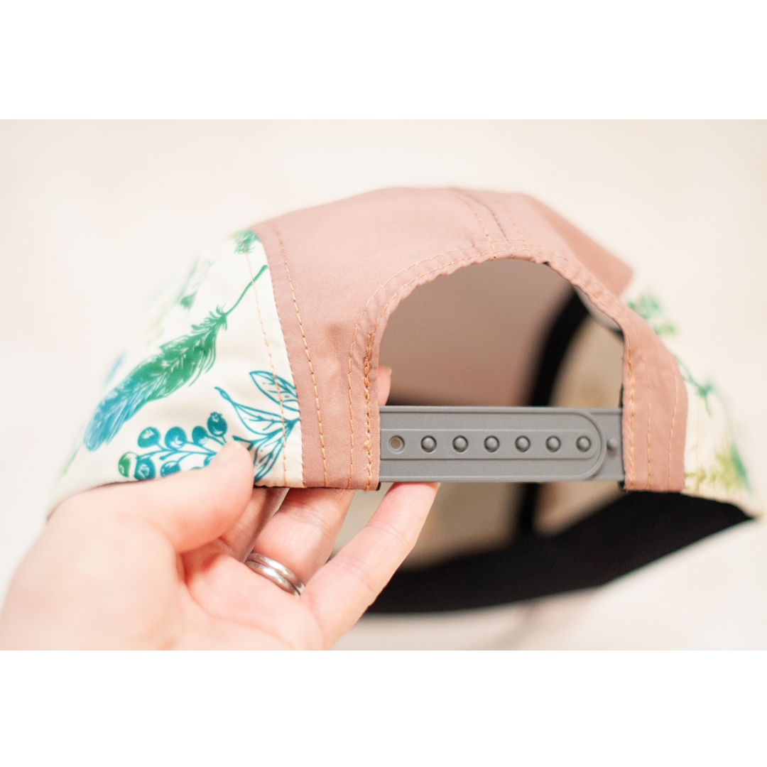 Hand holding a cap with a leaf pattern on the side against a neutral background