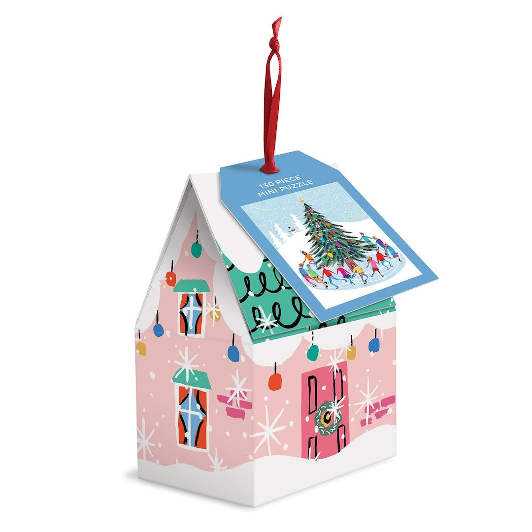 A Christmas-themed mini puzzle gift box shaped like a house, decorated with pink siding, snowflake patterns, colorful hanging ornaments, and a red hanging ribbon with a blue puzzle tag.