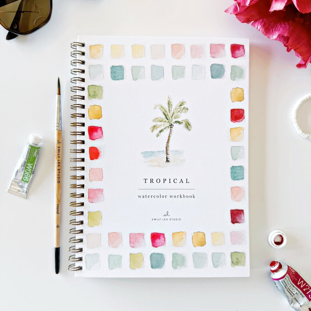 Tropical watercolor workbook with a paintbrush and paint tube on a white surface