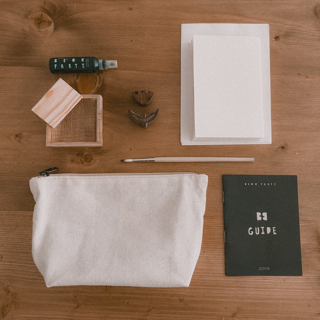 a bottle of ink, pine ink tray, 2 wooden blocks, cards, a paintbrush, canvas pouch, and block printing guide on a table 