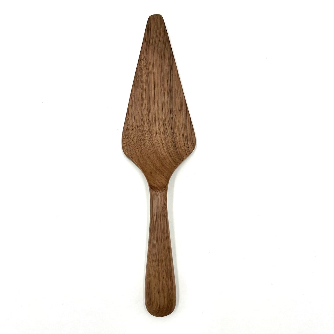 A single wooden serving spatula with a long handle and wide triangular blade, shown upright on a plain white background.