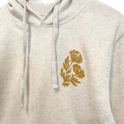 heather white hoodie with a gold floral design on the chest against a white background