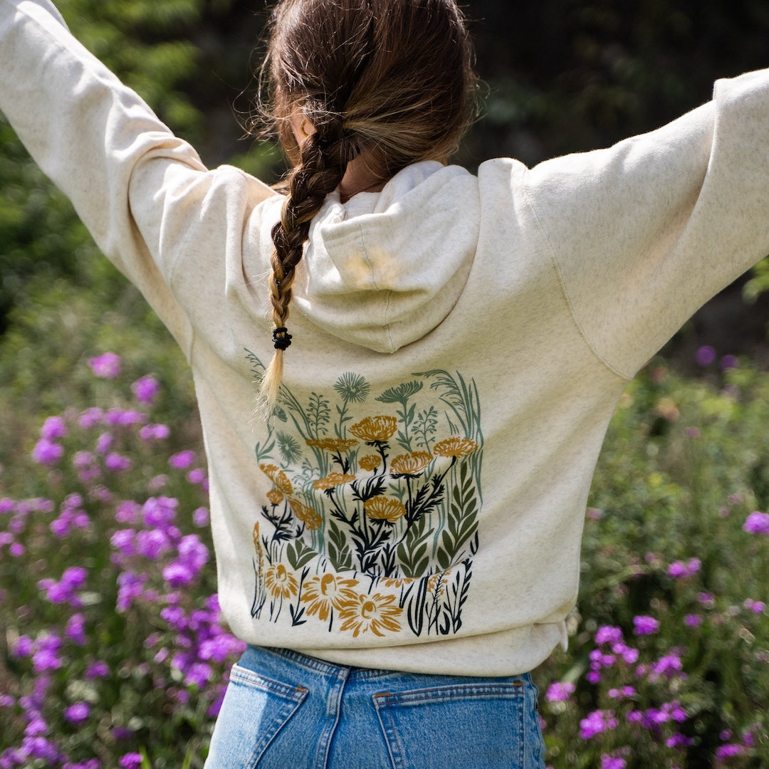 Person wearing a hoodie with floral design in a natural setting with flowers and greenery.