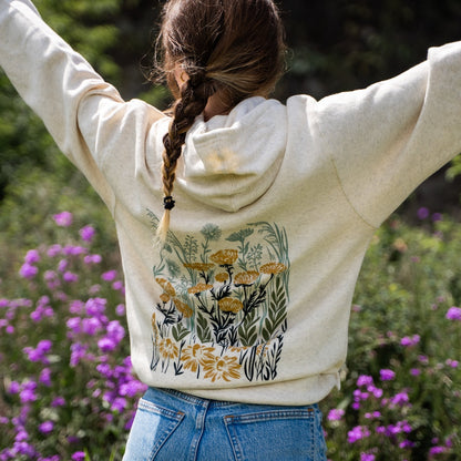 Person wearing a hoodie with floral design in a natural setting with flowers and greenery.