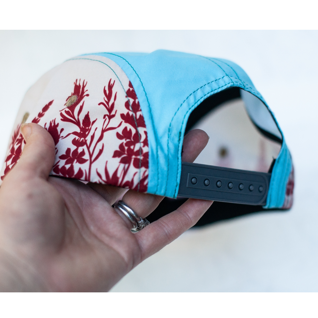 Hand holding a cap with floral pattern on one side and blue on the other, on a white background