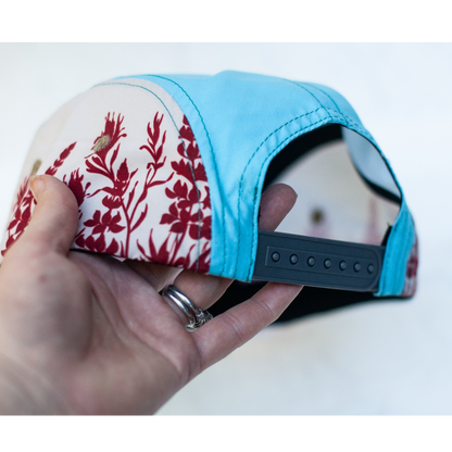 Hand holding a cap with floral pattern on one side and blue on the other, on a white background