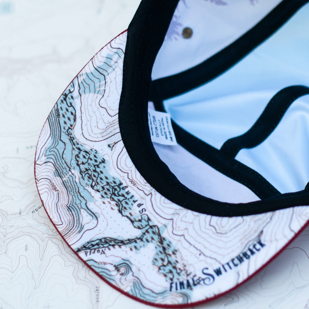 Close-up of a cap with a topographic design on the brim, featuring the brand 'Final Switchback'.