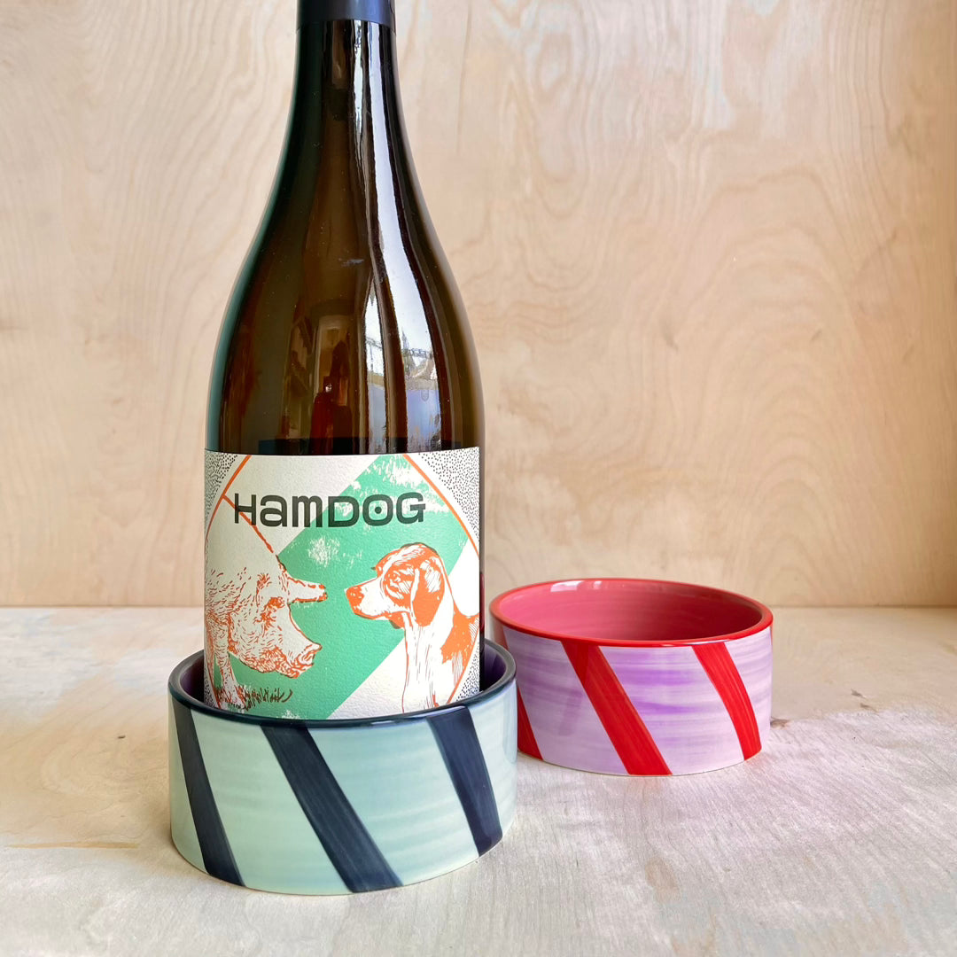 Wine bottle with a colorful label next to two ceramic bowls on a wooden surface.